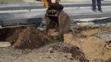 Sarı kazıcı kovası yol çalışması sırasında toprağı kazıyor..