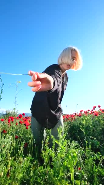 クリスタルクリアブルーの空に向かって踊るポピーフィールドの花を持つ少女 — ストック動画
