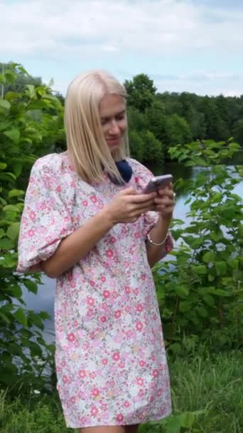 Young Blonde Floral Dress Stands Lake Looks Her Smartphone — Stock Video