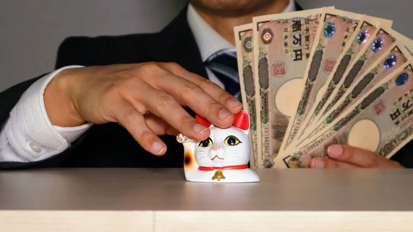 A businessman with a lot of money pats a beckoning cat