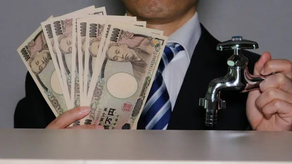Su musluğu ve banknotları olan bir iş adamı.