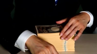Masasında bir tomar banknot düzenleyen bir iş adamı.