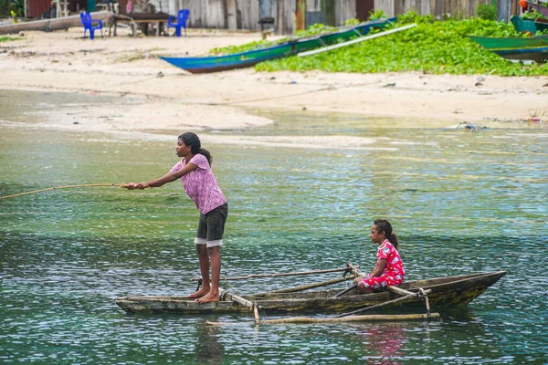 stock image Raja Ampat, West Papua, Indonesia - June 23th 2023: A portrait of two little girls fishing on a wooden canoe in a sunny day.