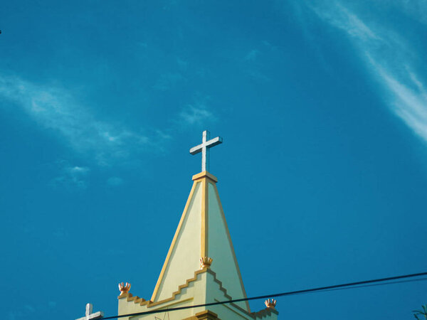 Church building roof with holy cross. Cloudy blue sky background. Minimalist exterior architecture design and detail.