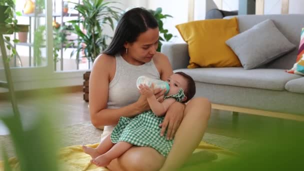 행복한 라틴어 엄마는 그녀의 거실에 그녀의 아기에게 병을주는 — 비디오