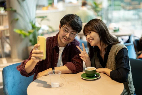 couple of friends having a coffee in a cafeteria while smiling they take a selfie