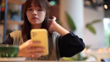 Modern şehir kafesinde akıllı telefon kullanan genç ve güzel bir Japon kadın. Cep telefonu konsantrasyonuyla mesaj atan Asyalı bir kadın.