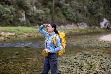 Doğanın ortasında elinde matarasıyla ufku tarayan genç bir kadın.