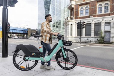 Kiralık e-motosikletiyle şehri gezen çekici İspanyol bir adam.