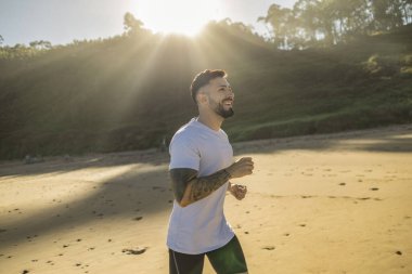 Güneş doğarken plajda koşan atletik İspanyol adam.
