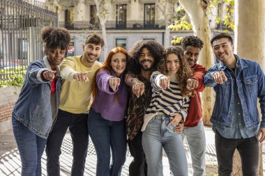 Bize katıl. Mutlu, neşeli, heyecanlı, kendine güvenen, güzel, genç yetişkin, çeşitli, modern günlük giysiler giyen, şehir caddesinde duran, gülümseyen ve sizi işaret eden arkadaşlar.