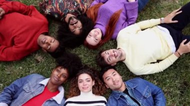 Çeşitli arkadaş grupları, kafaları bir arada ve elleri havada bir çemberin içinde çimlerin üzerinde uzanıyorlar. Irkçılığa hayır. dayanışma