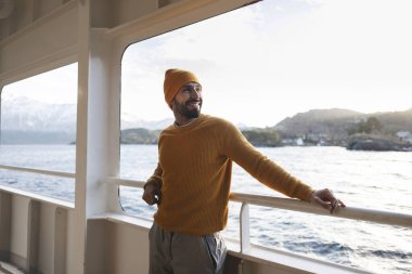 Tatilde manzaranın tadını çıkarırken fiyortlardan geçen bir teknede deniz macerasında model bir adam.