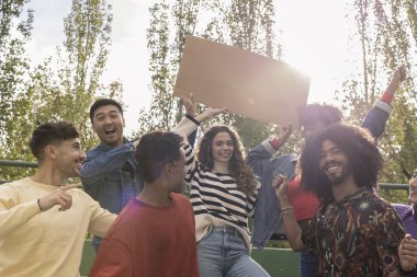 Çok ırklı bir grup genç arkadaş kahkahalarla tezahürat yapıyor ve akşam güneşi arka planda parlarken fotokopi alanı olan bir tabelayı işaret ediyorlar.
