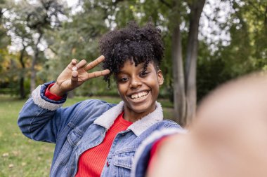 Genç ve şık Afro-Amerikan kadın selfie 'si. Barış işaretinde parmaklarıyla kameraya bakıyor.