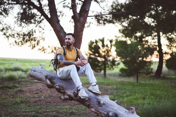 happy hispanic man contemplating the forest sitting on a log at sunrise
