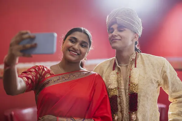 Indian bride and groom taking a selfie photo with their phone during Hindu ceremony