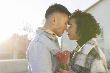 Çok ırklı aşıkların portresi gözleri kapalı ve kafaları gün batımında arka planda ve ellerinde bir buket gülle sevgililer günü konseptiyle birlikte.