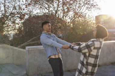 Çok ırklı bir çift şehirde el ele tutuşuyor, gün batımında dans ediyor.