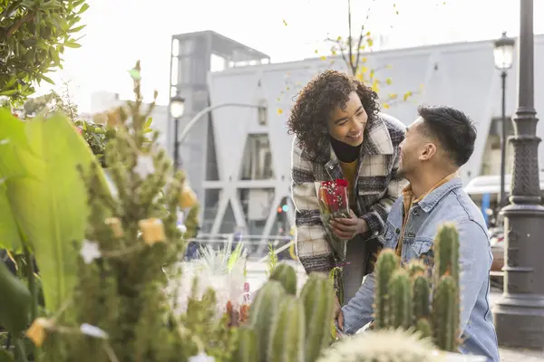 smiling multiethnic couple buying a bouquet of red roses for Valentine\'s Day at a florist in the metropolis