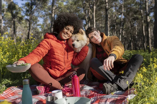 multiracial couple having a picnic in the woods with their dog