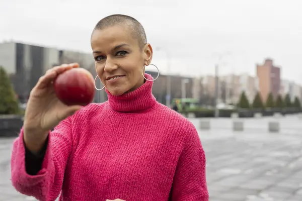 bald woman looking at camera with an apple in her hand - good nutrition prevents cancer