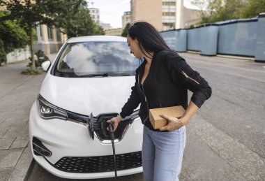 Genç bir kadın arabasını şarj istasyonuna takıyor.