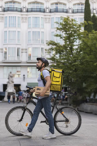 young adult man delivery man walks holding his bicycle lost through the city streets