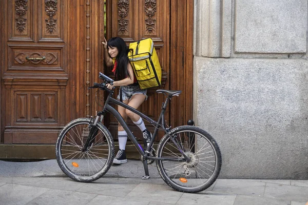 押しながら重いドアを開けるのに苦労している自転車を持つ配達女性 仕事での努力 — ストック写真