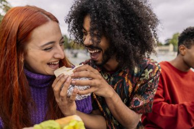 Etnik arkadaşlar bir sandviçi paylaşıp gülüyorlar