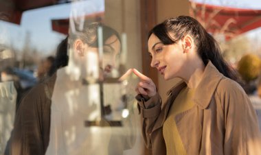 Güzel bir kadın hediye almak umuduyla bir mağazanın camını işaret ediyor.