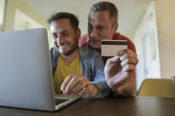 detail of credit card held by a homosexual couple shopping online with their laptop