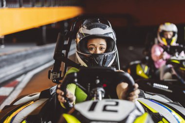 Karting pistinde elinde direksiyon tutan kasklı Latin bir kadın.