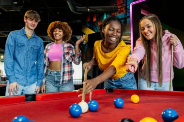Bir grup çok ırklı arkadaş toplara nişan alarak bilardo oynarken eğleniyor.