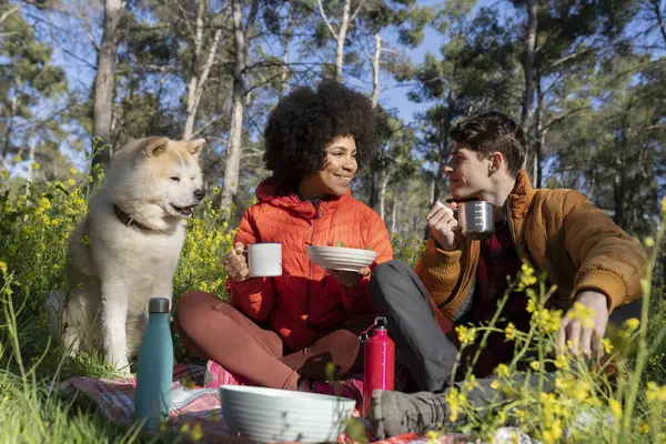 Multiracial couple with their dog on picnic in nature.