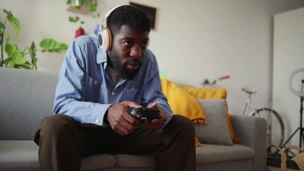Дружелюбный Африканский Американец Играющий Игровой Приставке Сидит Дома Диване Наушниках — стоковое видео