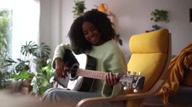 Mutlu Afrikalı Amerikalı kadın oturma odasında gitar çalıyor.