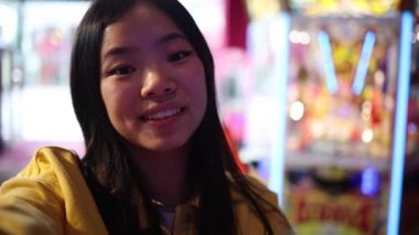 Video portresi etkisinde Asyalı bir kadın kameraya el sallıyor ve takipçileriyle konuşuyor. Oyun salonunda akıllı telefonuyla yaşıyor.