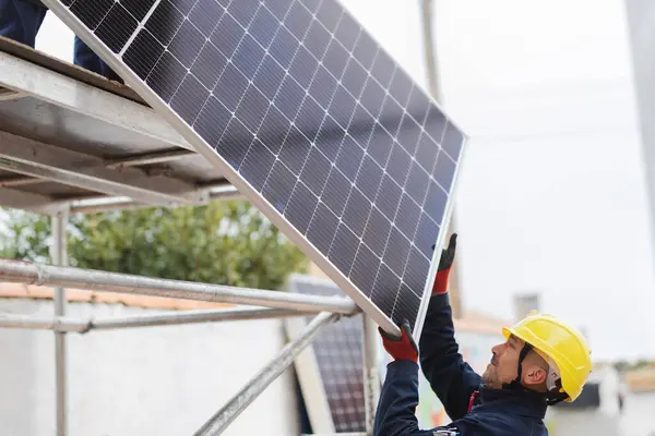 屋根に登るために太陽電池パネルを押すエンジニアの労働者 — ストック写真