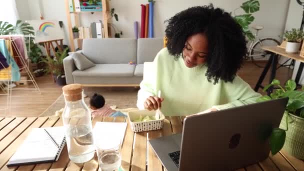 Afrikalı Amerikalı Kadını Laptopuyla Uğraşırken Öğle Yemeği Yerken Bebeğine Bakıyor — Stok video