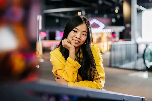 portrait of young woman of asian ethnicity leaning over pinball machine in arcade amusement game room