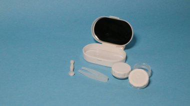 Mavi arka planda cımbız, tutucu ve kontak lensli konteynır