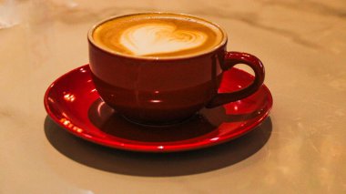 Tahta bir masanın üzerinde kalp şeklinde latte sanat eserleri olan bir fincan sıcak çikolatanın üst görüntüsü. Siyah seramik bir fincan ve çay tabağında sıcak bir içecek..