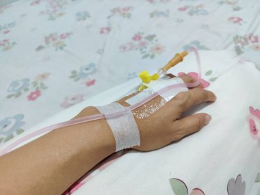 Bir kişinin sol elinin yakın plan görüntüsü. Elinin üstünden serum damlatılıyor. İçinde pembe vitamin sıvısı olan şeffaf serum tüpü. Sağlık için vitamin enjekte edin..