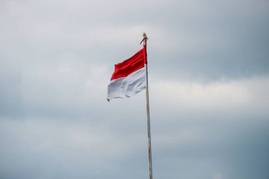 Rüzgarda dalgalanan Endonezya bayrağı ve arka planda kara bulutlar.