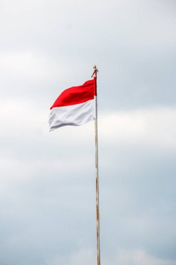 Rüzgarda dalgalanan Endonezya bayrağı ve arka planda kara bulutlar.