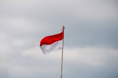 Rüzgarda dalgalanan Endonezya bayrağı ve arka planda kara bulutlar.