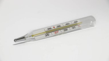 Beyaz yüzeyde klinik termometrenin yakın çekim görüntüsü. Tıbbi cam termometre vücut sıcaklığının 37 derece olduğunu gösteriyor. Beyaz arkaplanda cıva termometresi.