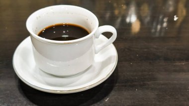 Tahta bir masanın üzerinde kalp şeklinde latte sanat eserleri olan bir fincan sıcak çikolatanın üst görüntüsü. Siyah seramik bir fincan ve çay tabağında sıcak bir içecek..