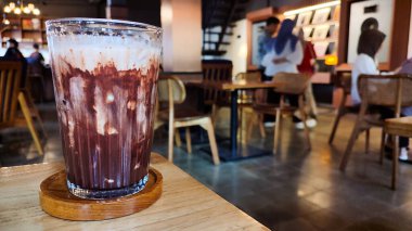 Buzlu çikolatayı yakın çekimde, modern kafede, ahşap masada servis edilir. Buzlu iç döşeme ahşap mobilyalar ve yumuşak ışıklandırma içeriyor..